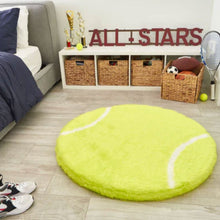A furry tennis shaped dogbed in front of a white drawers with trophies beside the grey bed and a basket full of toys and balls next to a grey bed and a pair of shoe