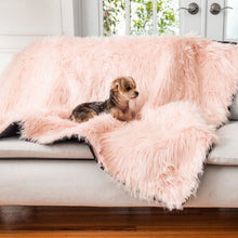 A morkie on a white couch laying on top of a blush pink waterproof dog blanket right next to a window