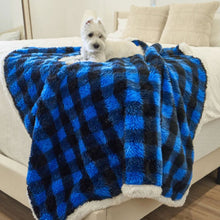 A white terrier on the edge of a white bed laying on waterproof black and blue checkered pattern dog blanket