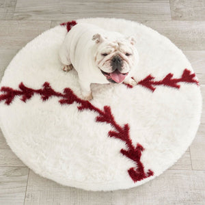 top view of a  white English bulldog sticking his tongue out sitting on a round baseball shaped dog bed 