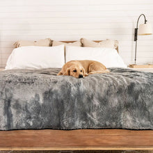 A golden retriever on bed with waterproof grey dog blanket and white and  brown pillows on the background and a white table lamp