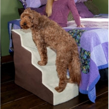 A furry brown dog standing on a four step dog stair next to a lady sitting in a blue bed on another angle