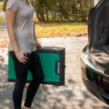 a close up image of a lady carrying a green tri fold dog ramp towards the car 