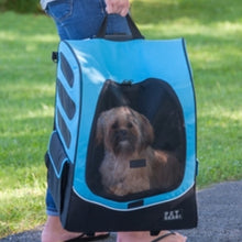 A close up image of a shih-tzu inside a blue dog traveler/carrier/stroller being held by a lady outdoors