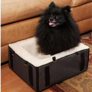 a black pomeranian sitting on the floor inside a booster car seat next to a leather couch