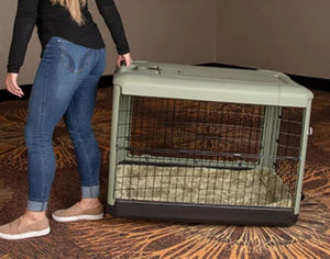 a woman dragging a sage colored steel dog crate on the floor with modern design