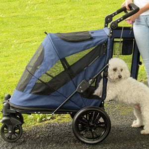 a white fluffy dog getting on a midnight blue dog jogger being guided by her owner in white at the park