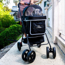 a lady pushing a black dog stroller with her cute dog inside it at the edge of the streets with green bushes on the other side