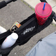 a close up image of a Universal Portable Stroller Organizer Tray attached to a stroller with a cup of water a phone and powder on it 
