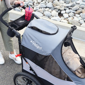 a woman pushing a grey dog stroller with a Universal Portable Stroller Organizer Tray attached in it  on the street