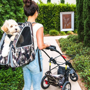 a lady walking in the garden with her dog on the back inside an army camo dog carrier and pushing a black stroller and an army camo organizer on it 