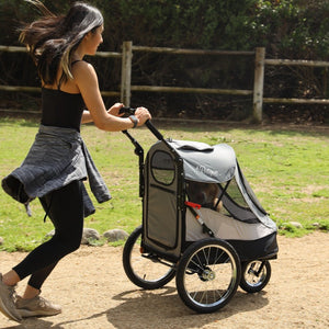 a woman running in the park pushing a space grey colored Dog Jogger Stroller with her dog inside it 