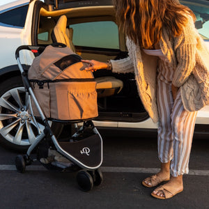 a lady poking her hands on a dog stroller next to a white car on the road 