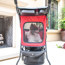 back view of a red stroller with black frames and organizer at the bottom with a happy dog inside the red stroller in front of a white house and a big potted plant