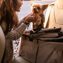 a happy lady paying with a tiny dog inside a dessert rose colored dog carrier on the car seat 
