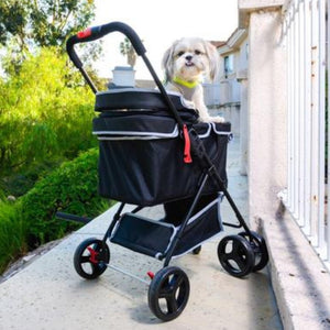 a cute little dog standing on a black dog stroller parked at the edge of the street with green bushes