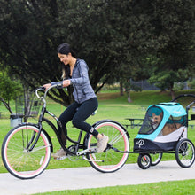 a lady ridding a bicycle with her dog inside a blue Dog Jogger Stroller attached to it  at the park