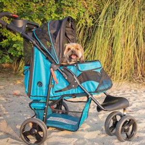 a happy dog inside a blue pet stroller facing right parked at the sands next to tall grasses