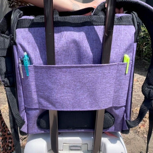 back view image of an orchid backpack dog carrier attached to a fully extended handle bar of a luggage carrier with pens inserted on it 
