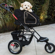 a happy dog inside a pepper colored dog carried laid on a stroller with black frames with organizer at the bottom next to some tall grasses