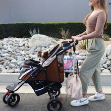a lady walking her dog inside a brown dog stroller on the street and her bag attached on the stroller using Pet Stroller Hooks