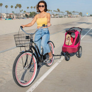 a lady riding a bicycle and a dog stroller connected to her bike with a happy dog inside it 