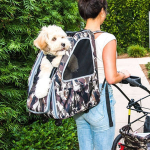 a lady walking in the garden pushing a stroller with her dog on her back inside an army camo dog carrier