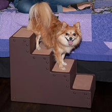 a small fluffy dog climbing down a brown dog stair next to a blue bed and a woman's leg on the background