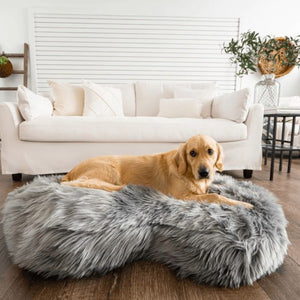 a golden retriever laying in a grey furry dog bed on the floor in front of a white couch in a modern living room with ornamental decorations