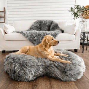 a golden retriever laying in a grey furry dog bed on the floor in front of a white couch with a grey dog blanket on it in a modern living room with ornamental decorations