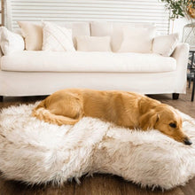 a golden retriever laying on a white fluffy dog bed in front of a white couch in an all white room with ornamental decorations at the back