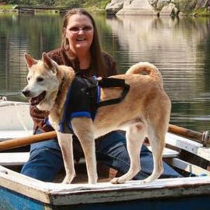 a lady with a glasses and her dog that is wearing a blue Walkabout Front End Harness rowing their boat on the lake 