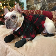 a french bulldog laying on a white couch wearing his christmas costume and a pair of Walkabout JAWZ Traction Booties next to a christmas tree