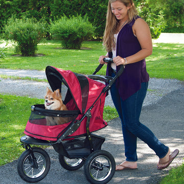 a woman walking her dog on a rugged red dog stroller in the park