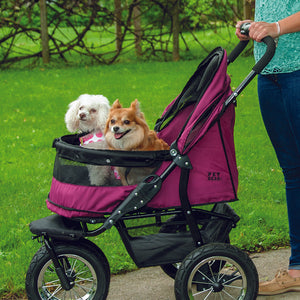 a woman walking her dog inside a berry colored dog stroller on the sidewalk