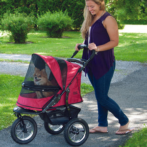 a woman walking her dog on a rugged red dog stroller in the park