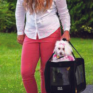 a close up image of a white dog peeking out of her dog car seat / carrier next to a lady wearing a pink jeans outdoors