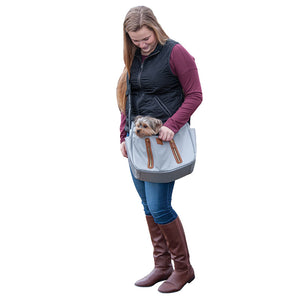a lady wearing a black vest and marron sweatshirt carrying her dog on a fog Sling Pet Carrier Purse