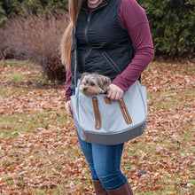 a lady wearing a black vest and marron sweatshirt carrying her dog on a fog Sling Pet Carrier Purse