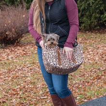 a lady wearing a black vest and marron sweatshirt carrying her dog outdoors in a jaguar printed Sling Pet Carrier Purse