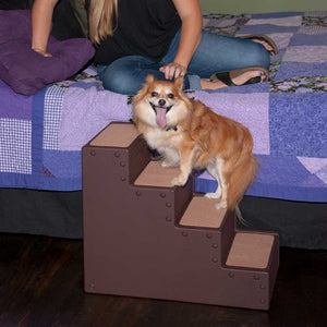 a lady sitting on the bed with blue sheets watching her dog standing on a four step chocolate pet stairs 